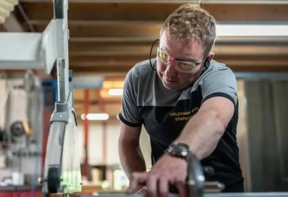 Medewerker van Veldkamp RVS die met beschermende bril een RVS onderdeel nauwkeurig bewerkt aan een machine, gericht op precisie en afwerking in de werkplaats.