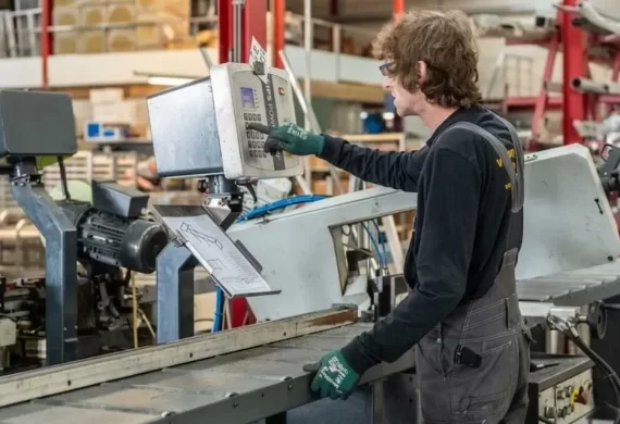 Medewerker van Veldkamp RVS die een metaalbewerkingsmachine instelt en bedient via het bedieningspaneel, met een technische tekening zichtbaar voor nauwkeurige productie.